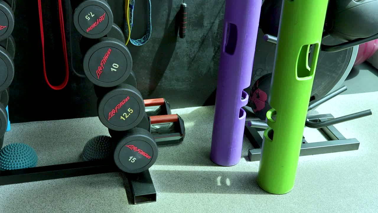 Camera pans across organized gym equipment, weights, resistance bands, and exercise tools in bright lighting