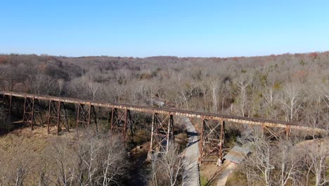 Toma-Aérea-Avanzando-A-Lo-Largo-De-Una-Carretera-Hacia-El-Caballete-Del-Ferrocarril-Pope-Lick-En-Louisville-Kentucky,-Con-Un-Bosque-Al-Fondo-En-Un-Día-Soleado