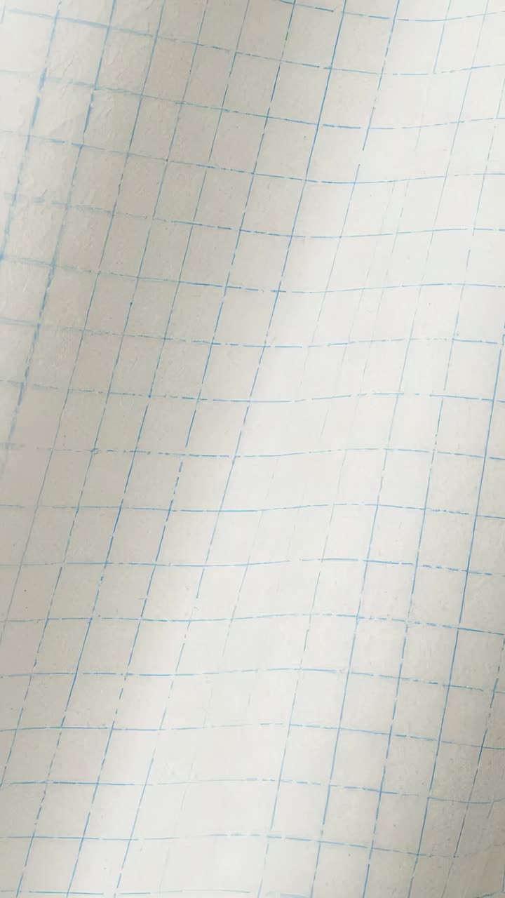Vertical video: Cam panning over graph paper on surface with blue grid, revealing creases for study