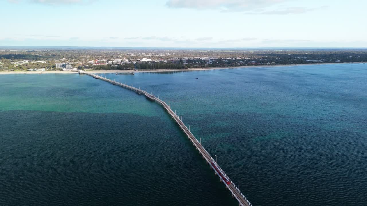 Drone zooming out over Busselton Jetty pier as the tourist train drives along the tracks