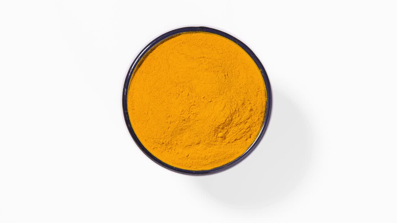 Curcuma turmeric spice powder in round bowl on white background, seamless loop