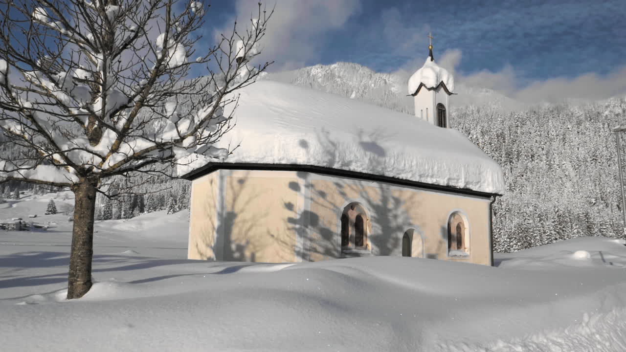 Gimbal shot showing a snowy landscape in in the sunshine of the Tyrol, Austria and revealing a snow covered tiny chapel in Lechaschau