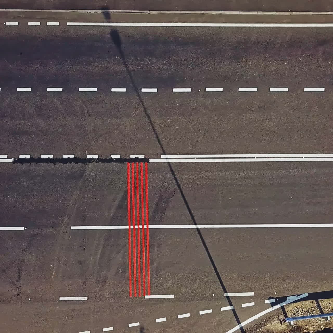 Few long vertical red stripes painted on one side of the road surface and cars passing. Aerial view of wide asphalt road divided into two opposite sides for cars. Camera moves right