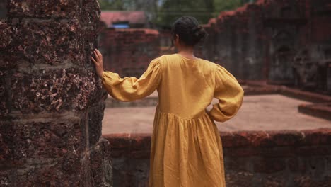 Una-Mujer-Con-Un-Vestido-Amarillo-Explora-Antiguas-Ruinas-De-Piedra.