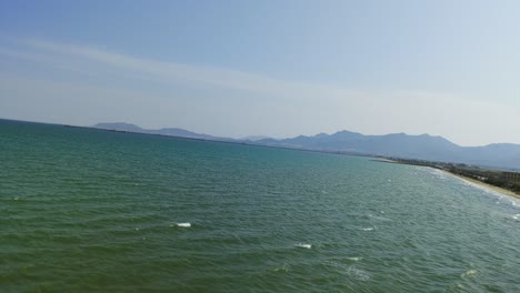 aerial drone shot flying over sea along coastline near pula, mountains in background, sardinia, italy