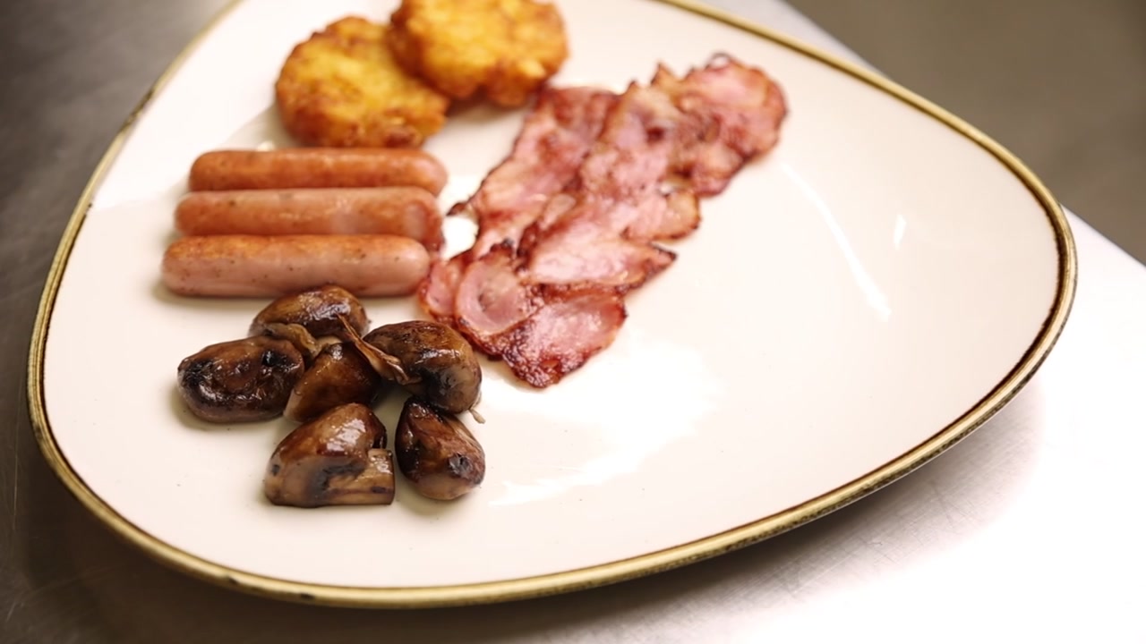 Piatto di colazione all'inglese completa con pancetta, salsicce, hash brown e funghi