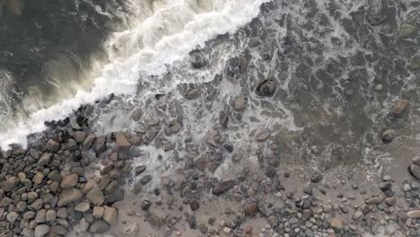 Overhead-orbital-shot-of-gentle-shoreline-waves-crushing-into-the-rocky-coast