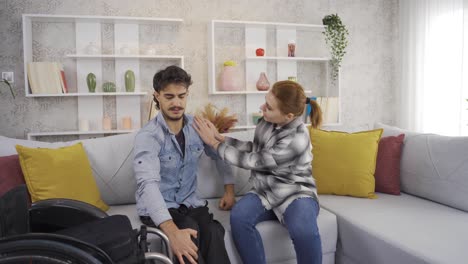 una chica ayuda a su novio discapacitado a salir de la silla de ruedas en casa.