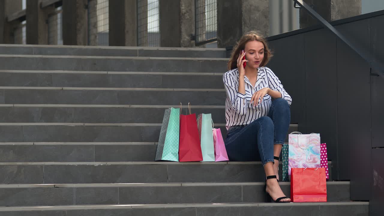 chica sentada en las escaleras con bolsas hablando en el teléfono móvil sobre la venta en el centro comercial en black friday