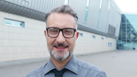 vista de cerca del hombre de negocios canoso con gafas y mirando la cámara en la calle