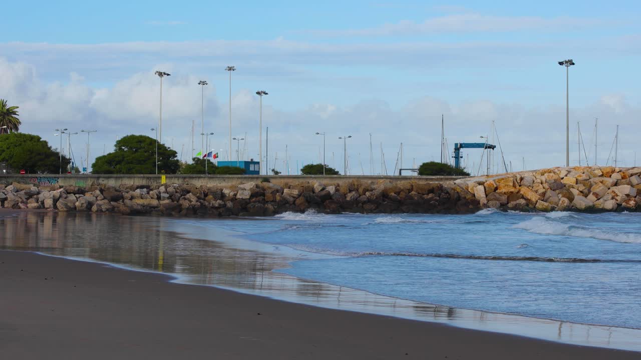 puerto deportivo con barcos y algunas olas rompiendo en la playa de lisboa, portugal.