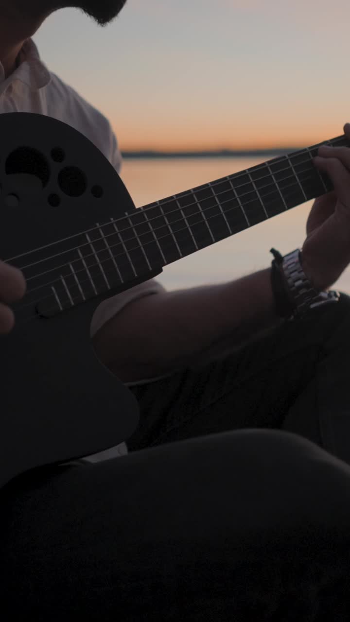 Gra na gitarze o zachodzie słońca nad wodą