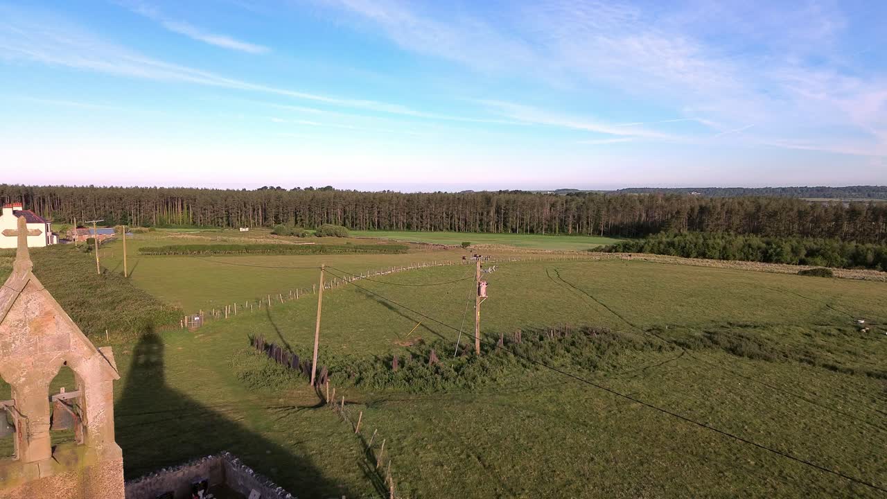 St Peters church bell tower aerial view establishing rural Welsh Newborough forest at sunrise