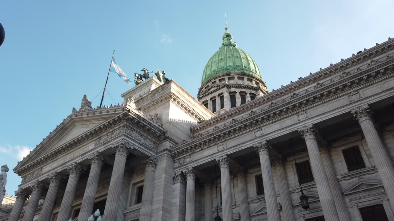 Perspectiva de ángulo bajo del Palacio del Congreso Nacional Argentino en Buenos Aires. Fachada neoclásica detallada y cúpula verde bajo un cielo azul claro. Edificio gubernamental icónico.