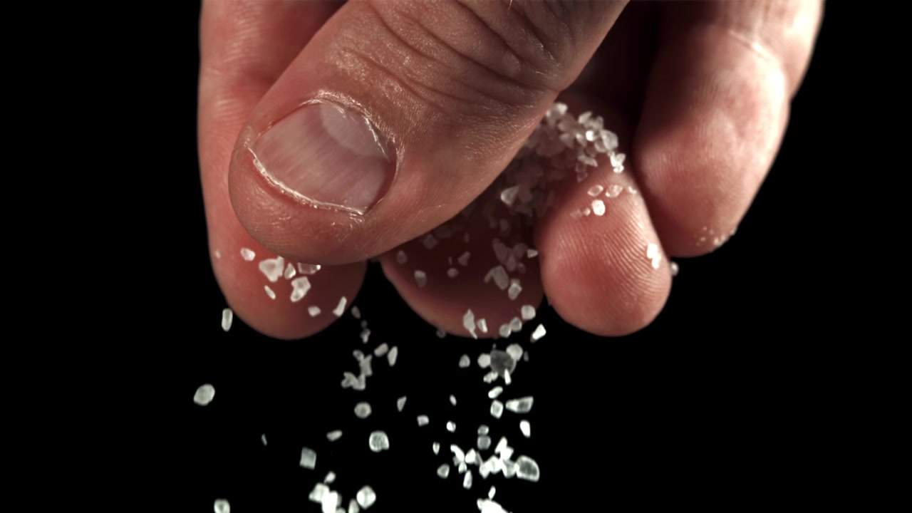 Hand Sprinkling Coarse Salt in Slow Motion on Black Background