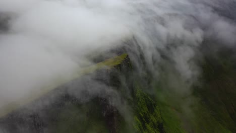 clouds rolling over steep faroe islands hilltops on overcast day, aerial view