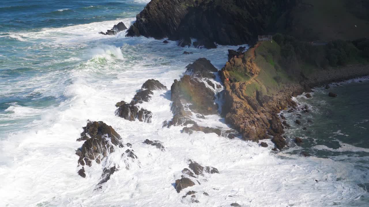 Dynamic aerial view of powerful ocean waves crashing against rocky cliffs in Byron Bay, Australia, under bright daylight