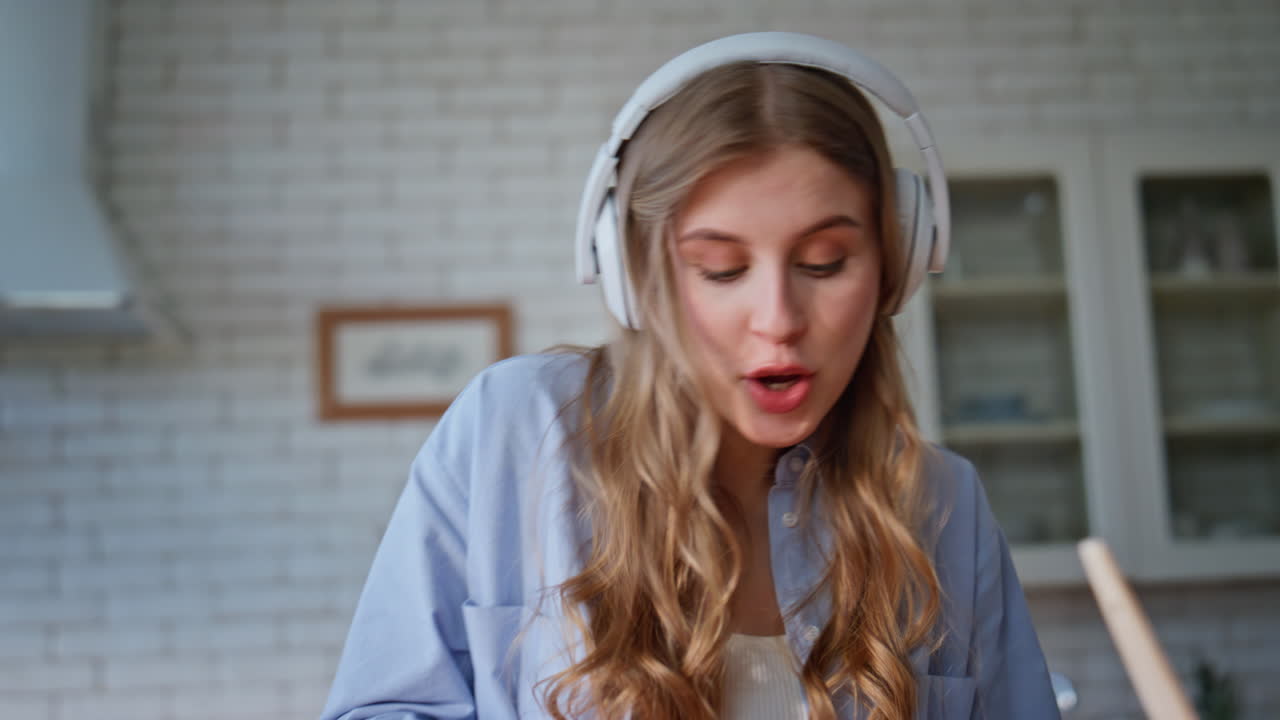 Dancing woman preparing breakfast in kitchen wearing wireless headphones closeup