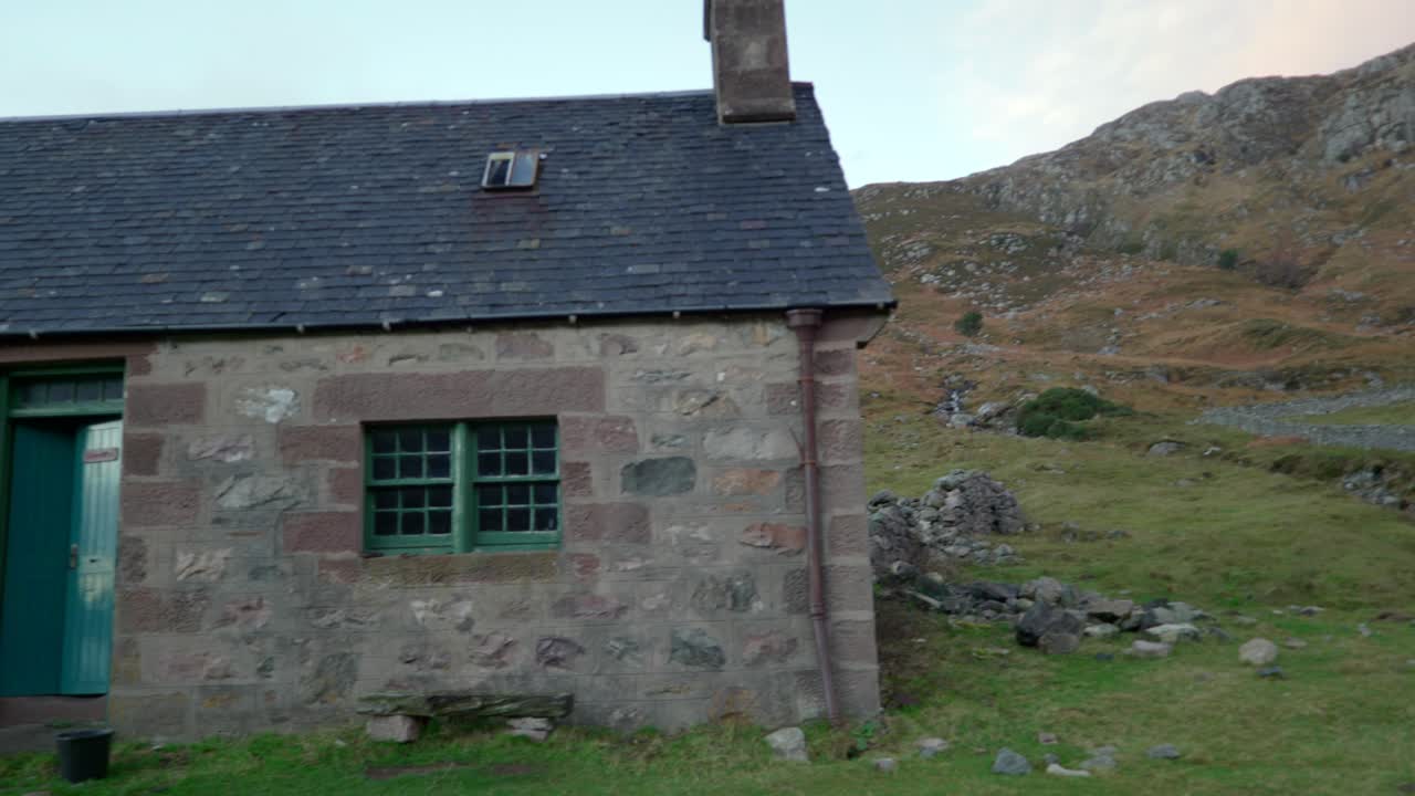 alejándose de la cresta de una montaña en el fondo, un antiguo edificio de piedra aparece en una cañada remota en la escocia rural