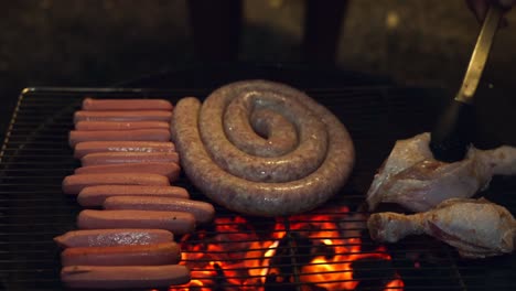 barbecue of sausages, and man adding chicken pieces to the grill, evening gathering at home with family and friends