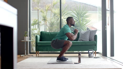 exercising at home, man doing squats on yoga mat with kettlebell nearby