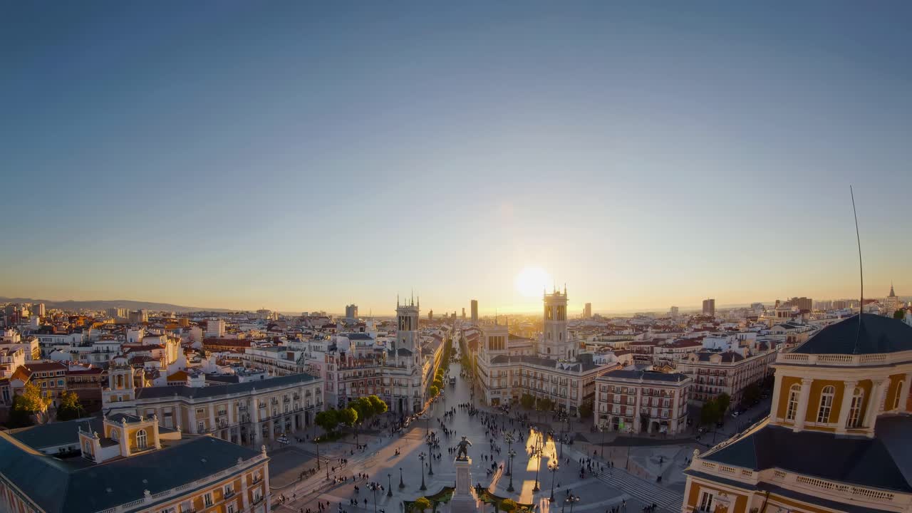 Un video aereo cattura un paesaggio urbano al tramonto con un obiettivo grandangolare, mostrando una vivace piazza