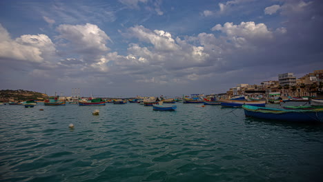 boats docked or anchored in pretty bay at marsaxlokk, malta - dreamy cloudscape time lapse