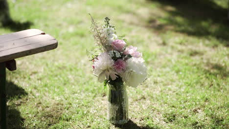 Rustic-floral-arrangement-in-a-glass-jar-on-the-grass-beside-a-wooden-bench