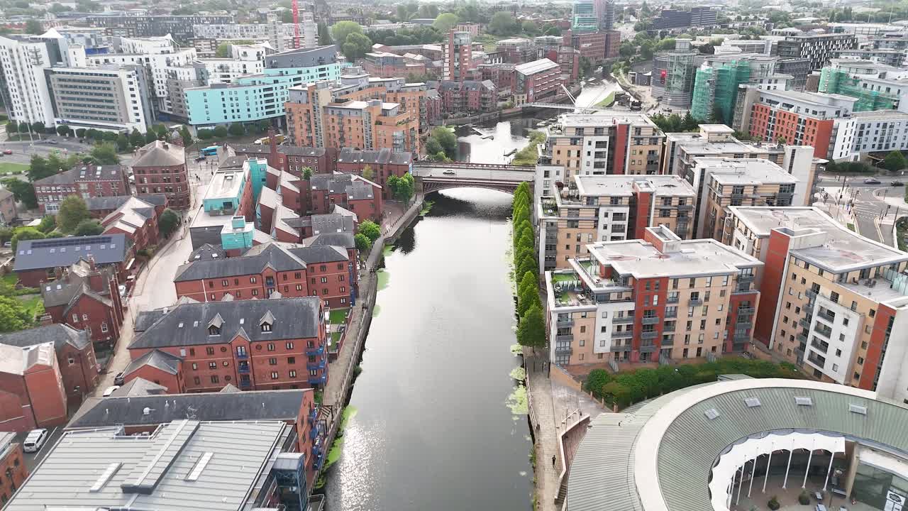 Drone footage glides above the River Aire in Leeds, revealing Victorian buildings, modern apartments, and bridges under soft daylight with smooth camera movement