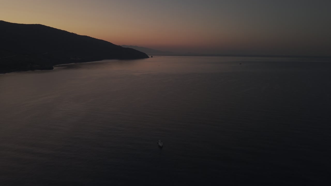 Aerial drone rising shot over a sailboat on calm waters at sunrise in the Aegean Sea near Lesbos, Greece.