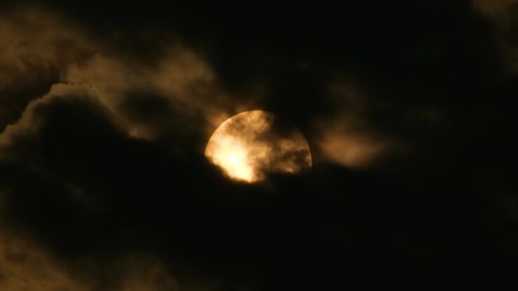 Big sun rises through dark clouds and hides behind the clouds again