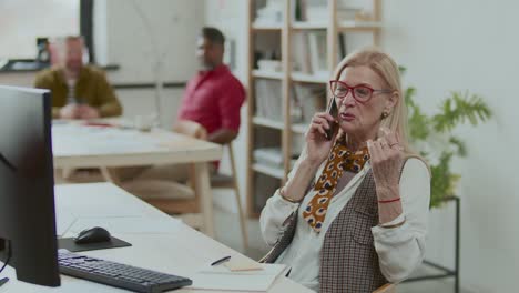 senior businesswoman talking on mobile phone at desk in modern office