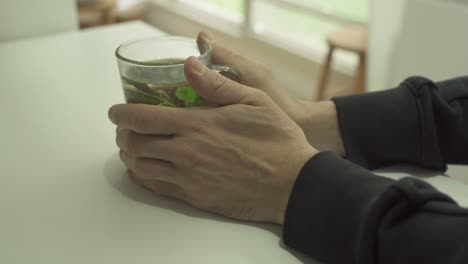 man's hands hold hot herbal tea glass in a cold day