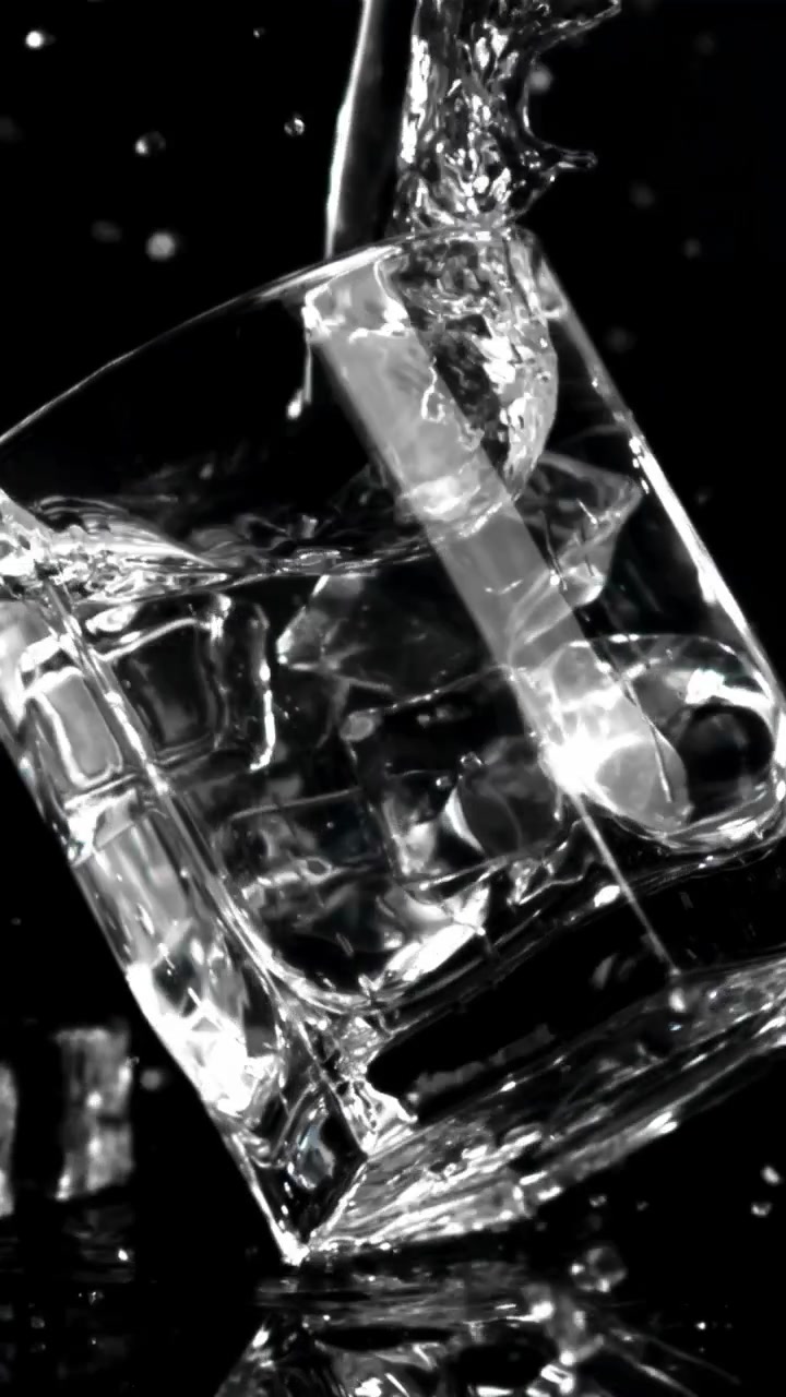 Acqua che si versa al rallentatore in un bicchiere con cubetti di ghiaccio