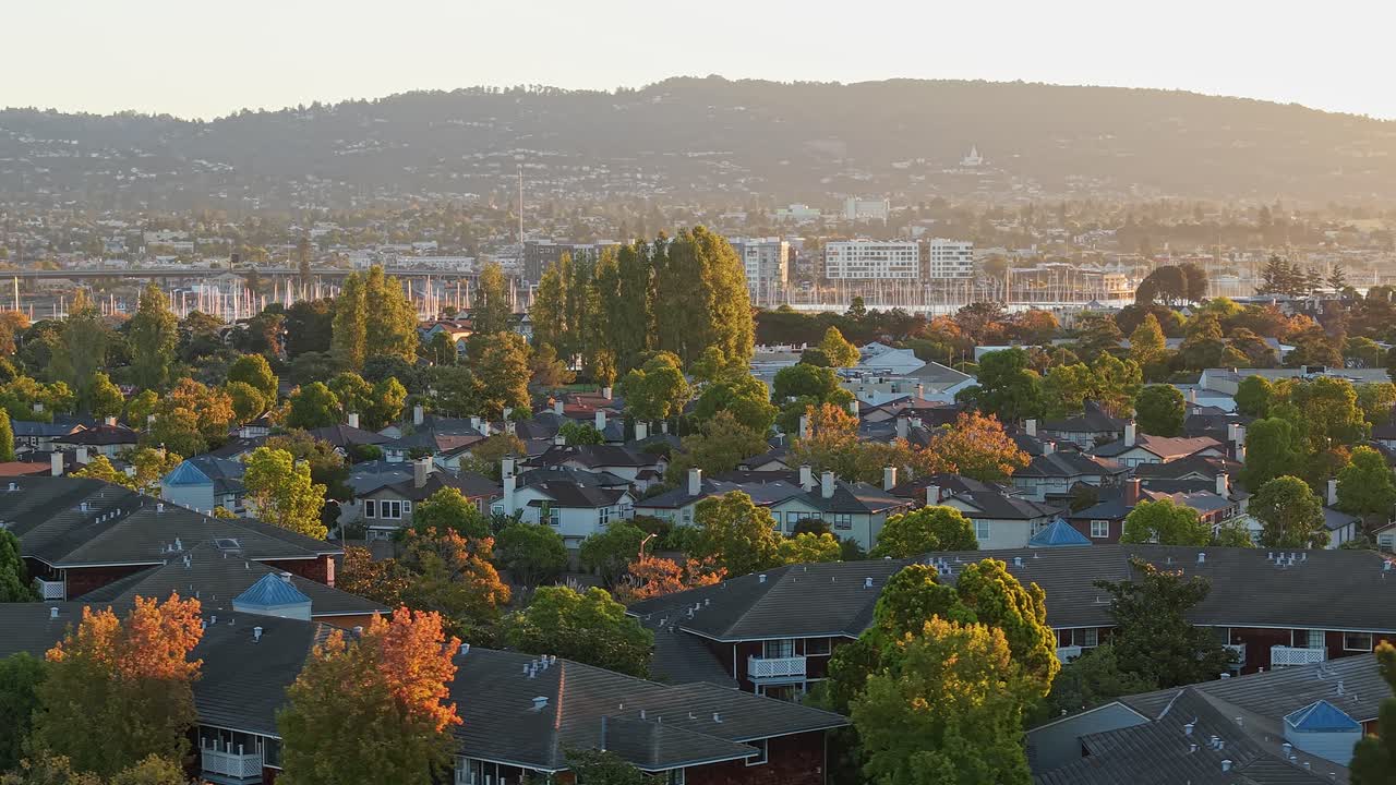 Panning drone views of West Alameda highlight its waterfront homes, sailboats, and the shimmering expanse of Oakland in the distance