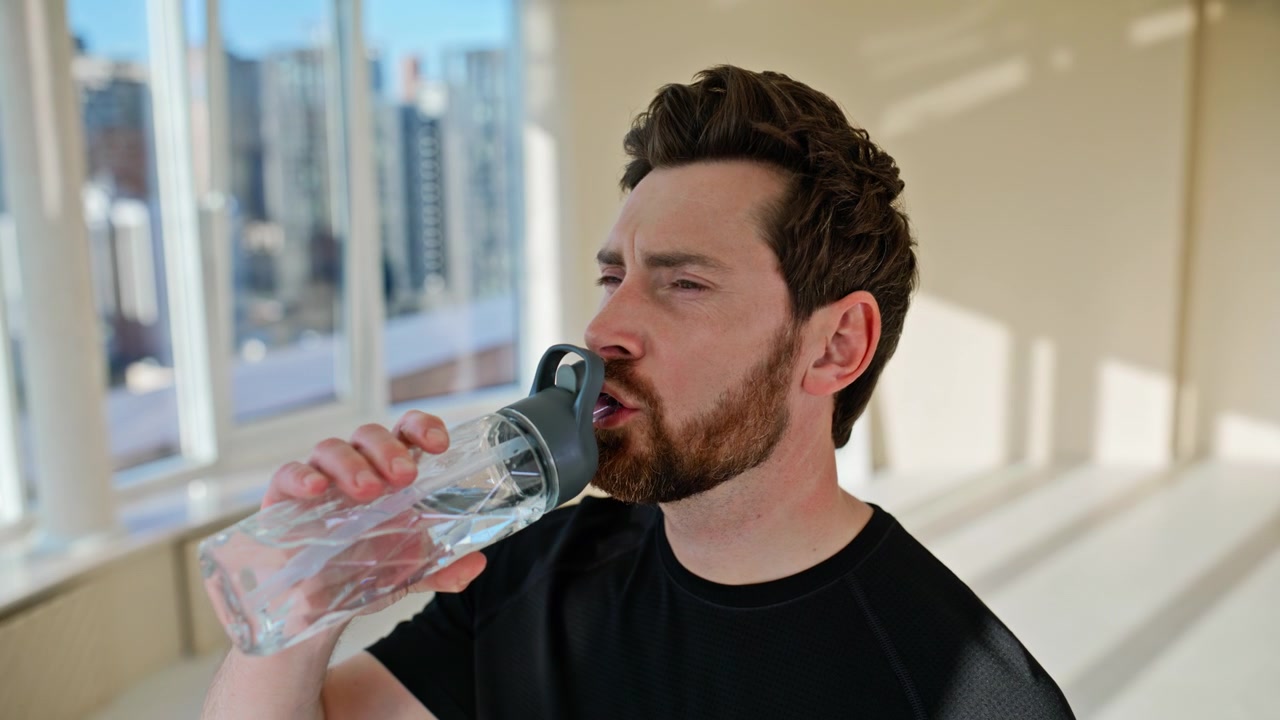 Thirsty man drinking water bottle after workout. Close up tired sportsman rest.