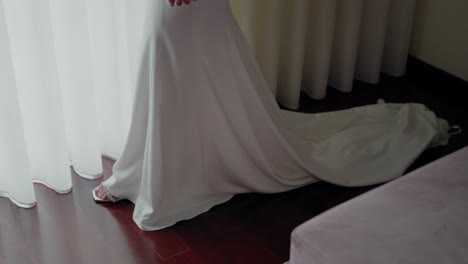 flowing white wedding dress with a long, elegant train cascading across a wooden floor near sheer curtains