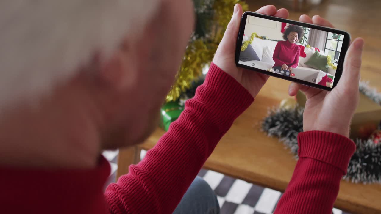 hombre caucásico con sombrero de santa usando un teléfono inteligente para una videollamada de navidad, con una mujer en la pantalla