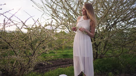 Una-Tierna-Dama-Vestida-De-Blanco-Está-Parada-En-Un-Jardín-Floreciente-En-Primavera,-La-Belleza-De-La-Mujer-Y-La-Naturaleza