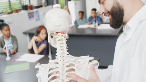 diverse male teacher and happy schoolchildren studying skeleton in biology class