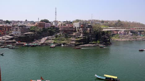 Stadt-Am-Ufer-Des-Heiligen-Flusses-Mit-Touristenfähren-Am-Morgen.-Das-Video-Wurde-Am-10.-März-2024-In-Omkareshwar-Khandwa,-Madhya-Pradesh,-Indien,-Aufgenommen