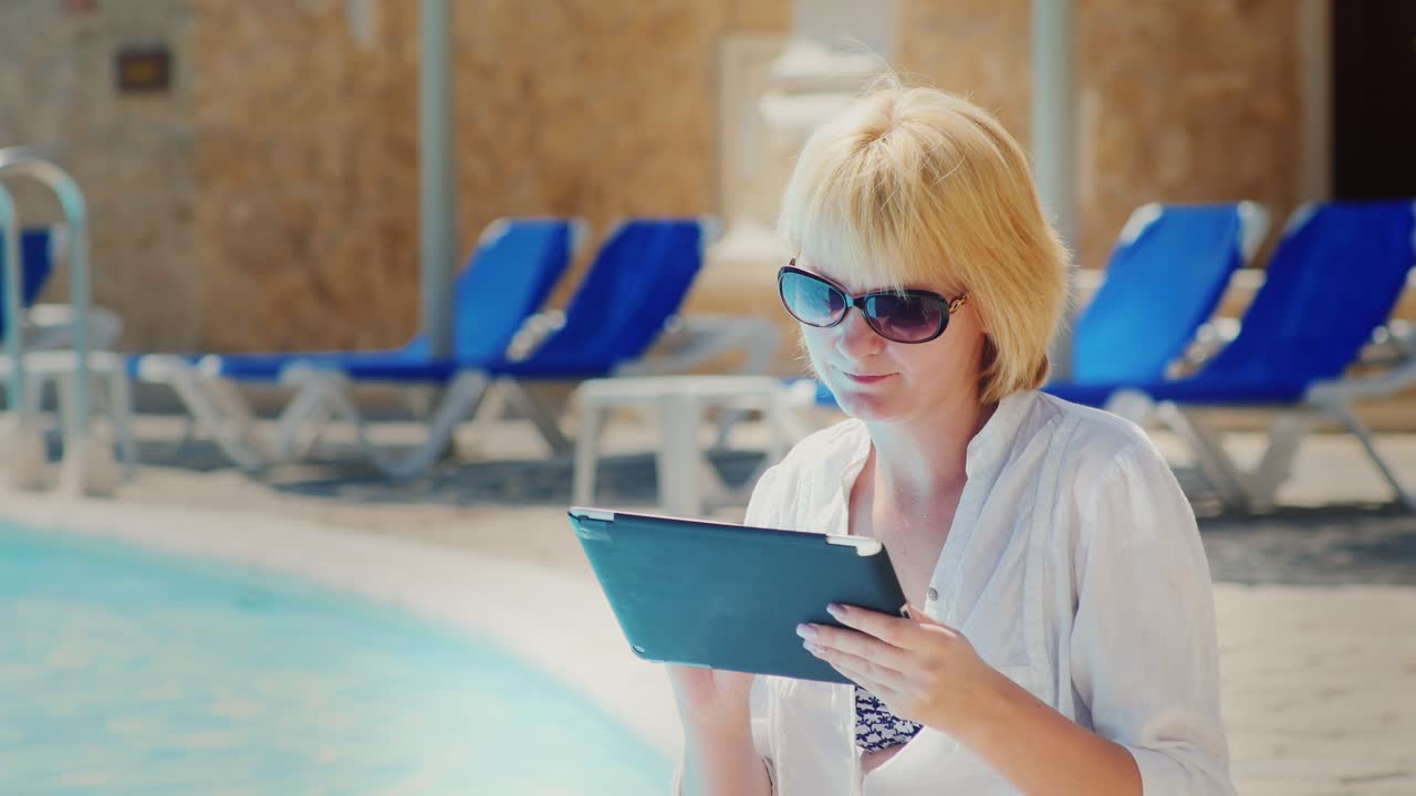 태블릿을 즐기는 수영장 옆에서 휴식을 취하는 여성