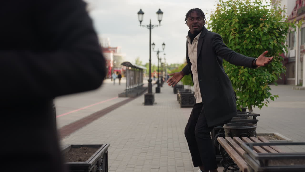 Oskarp vy av människor i rörelse i bakgrunden på en stadsgata med en kvinna som skyndar mot en sittande man som håller en smartphone, vilket fångar rörelsen och den livliga atmosfären i en modern livsstil i en naturlig miljö.
