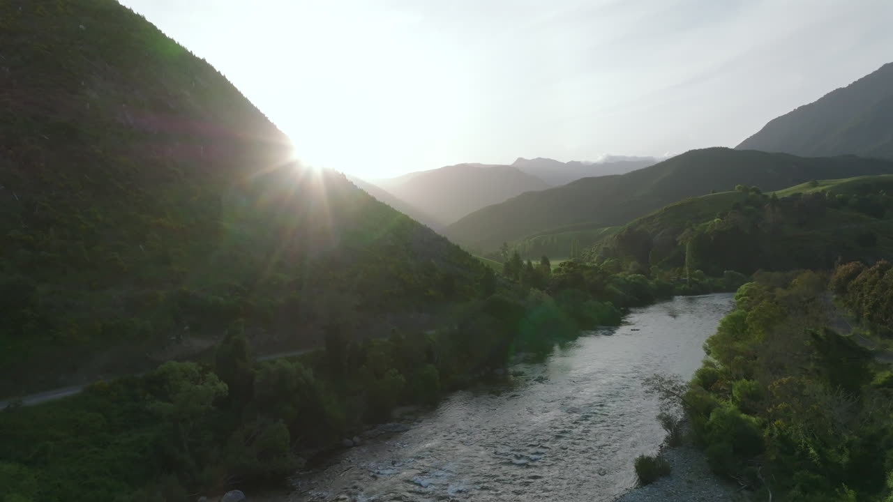 Drone ascending over the Motueka river to reveal the sun low in the sky during sunset, New Zealand