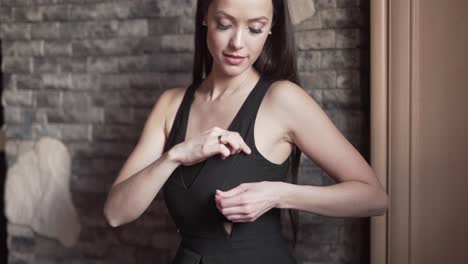 Young-Caucasian-Mother-With-Long-Black-Hair-Checking-Zipper-on-Her-Black-Dress-for-Breast-Feeding-in-Front-Of-The-Wall