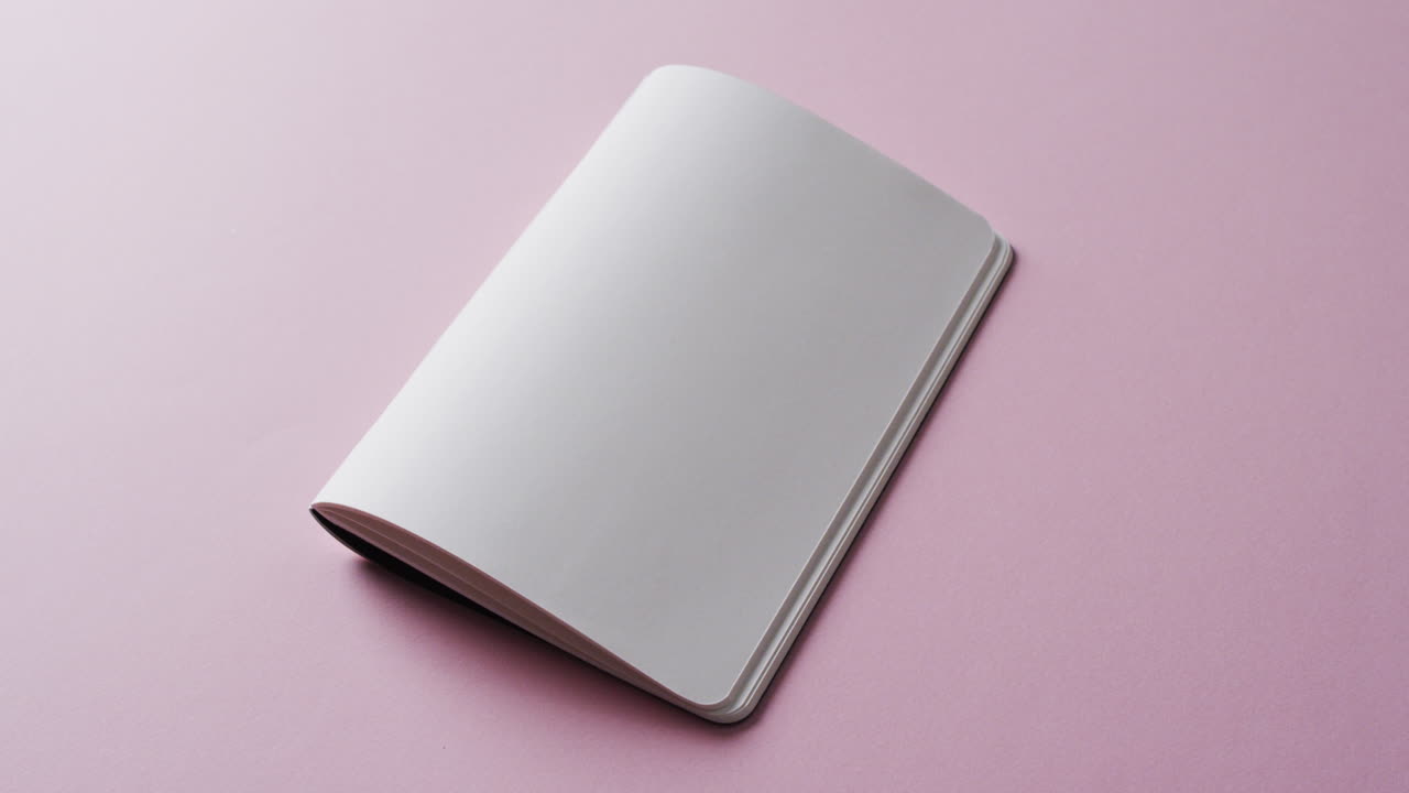 Close up of open blank book with copy space on pink background in slow motion