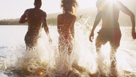 young adult friends on vacation running into lake at sundown