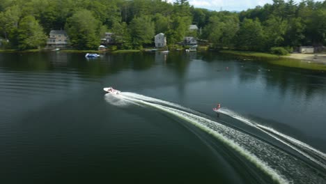 an outdoor shot of a man water skiing at a clear lake can be seen with many lush, green trees in the background, partly overcast with light thunderclouds