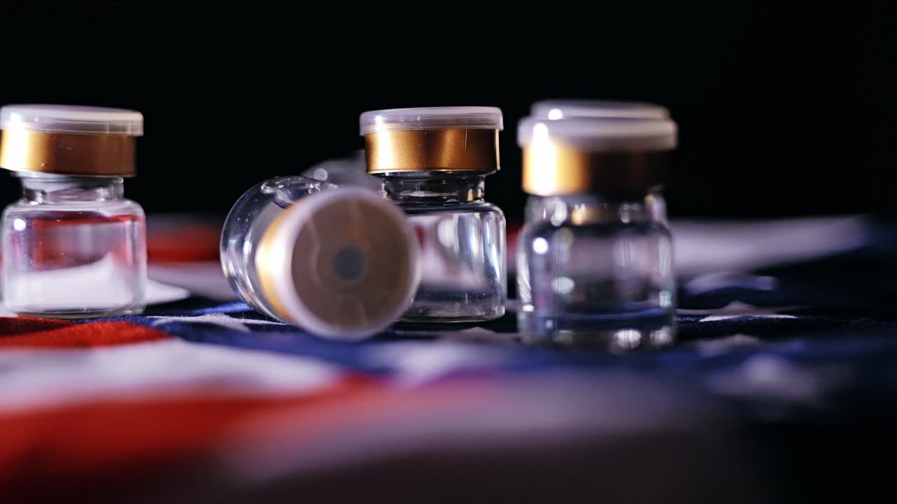 Rotating vaccine vials on flag reflect capitalism, biotech, economic dominance