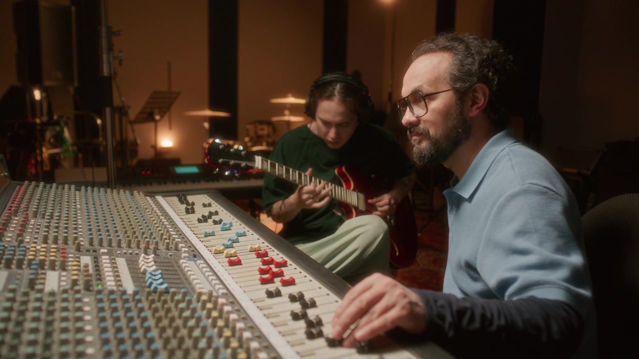 Audio Engineer Adjusting Mixing Console while Musician Playing Guitar in Studio